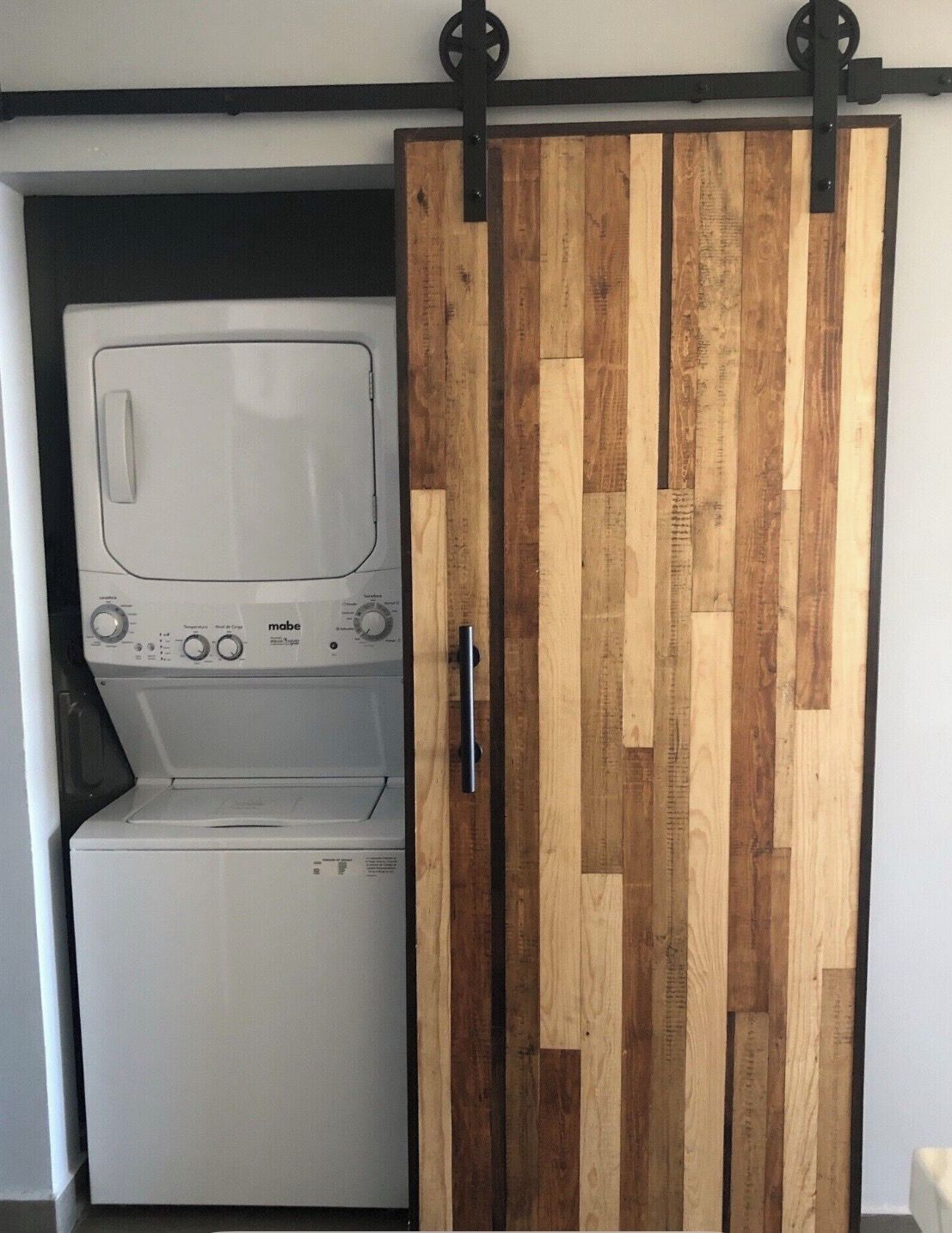Une buanderie équipée d’un lave-linge et d’un sèche-linge, avec une porte coulissante en bois et une poignée en métal.