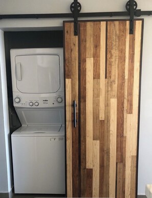 A laundry room with a washing machine and dryer, a wooden sliding door, and a metal handle. - 🌴MODERN 1 BEDROOM OCEANFRONT CONDO WITH BREATHTAKING VIEWS SONORAN SUN RESORT🌴 (Puerto Peñasco)