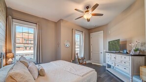 A bedroom with a bed, a ceiling fan, a dresser, a TV, and a window with curtains.