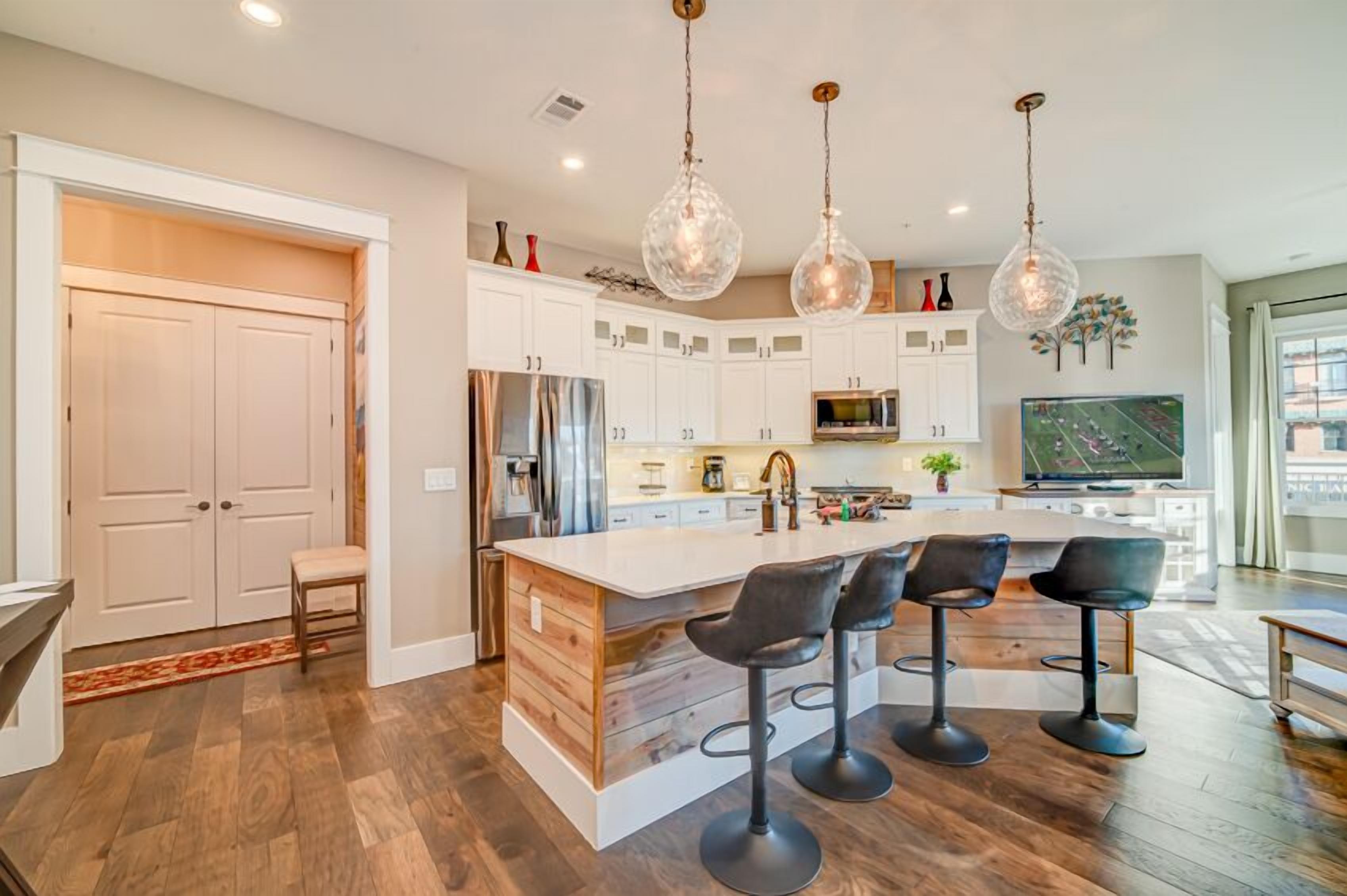 A modern kitchen with white cabinets, a large island with bar stools, stainless steel appliances, and pendant lighting.