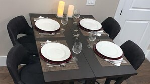 A dining table set with white plates, red rimmed glasses, and silverware, surrounded by black chairs.