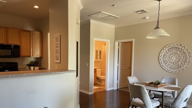 A modern kitchen with wooden cabinets, a microwave, and a countertop. There is a dining area with a table and chairs, and a decorative wall piece.