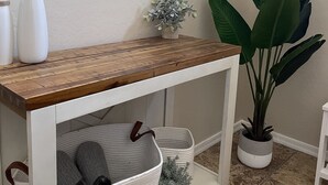 A white console table with a wooden top, white baskets, and a potted plant.