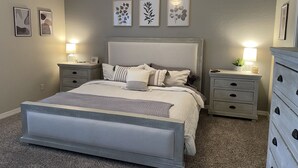 A bedroom with a large bed, two bedside tables, a dresser, and wall art.