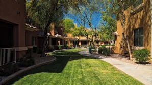 A courtyard with a well-maintained lawn, trees, and a pathway leading to a building with a tiled roof.