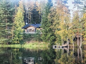 A cabin with a dock extending into a calm lake, surrounded by dense forest.