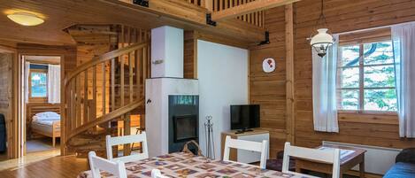 A wooden cabin interior with a dining area, a fireplace, a TV, and a staircase.