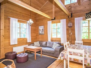 A cozy cabin interior with a sofa, table, and chairs, wooden walls, and large windows.