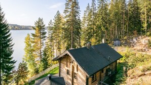 Une cabane dotée d’un toit en pente, entourée de grands arbres et bordée par un lac.