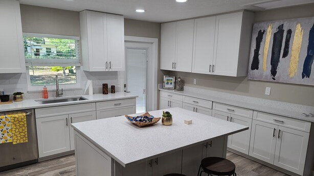 A modern kitchen with white cabinets, a large island with stools, a window with a view, and a painting on the wall. - Quiet Neighborhood and close to all Tampa offers (Tampa)
