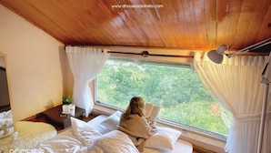 Una habitación con una cama, una ventana con cortinas, una mesita de noche con lámpara y vistas a espacios verdes.