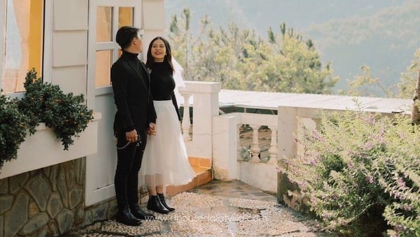Una pareja parada frente a un edificio con vistas a las montañas.
