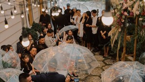 Un grupo de personas reunidas en un espacio interior, algunas sosteniendo paraguas transparentes.