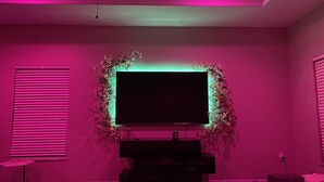 A bedroom with a large TV mounted on the wall, surrounded by a floral arrangement. - Walk to Super Bowl LV! Grand Spanish Style Home (Tampa)