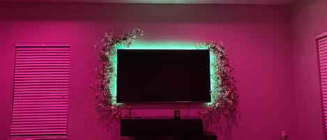 Un dormitorio con un televisor grande montado en la pared, rodeado de un arreglo floral.