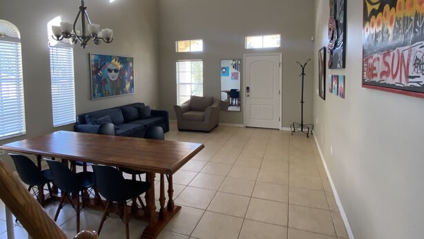 A spacious living area with a dining table, sofas, and a chandelier. There are multiple windows allowing natural light and a door leading to another room. - Walk to Super Bowl LV! Grand Spanish Style Home (Tampa)