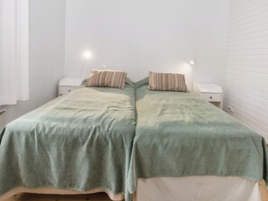 Ein Doppelzimmer mit zwei Betten, jeweils ausgestattet mit einem gemusterten Überwurf und Kissen, einem Nachttisch und einer Wandleuchte.