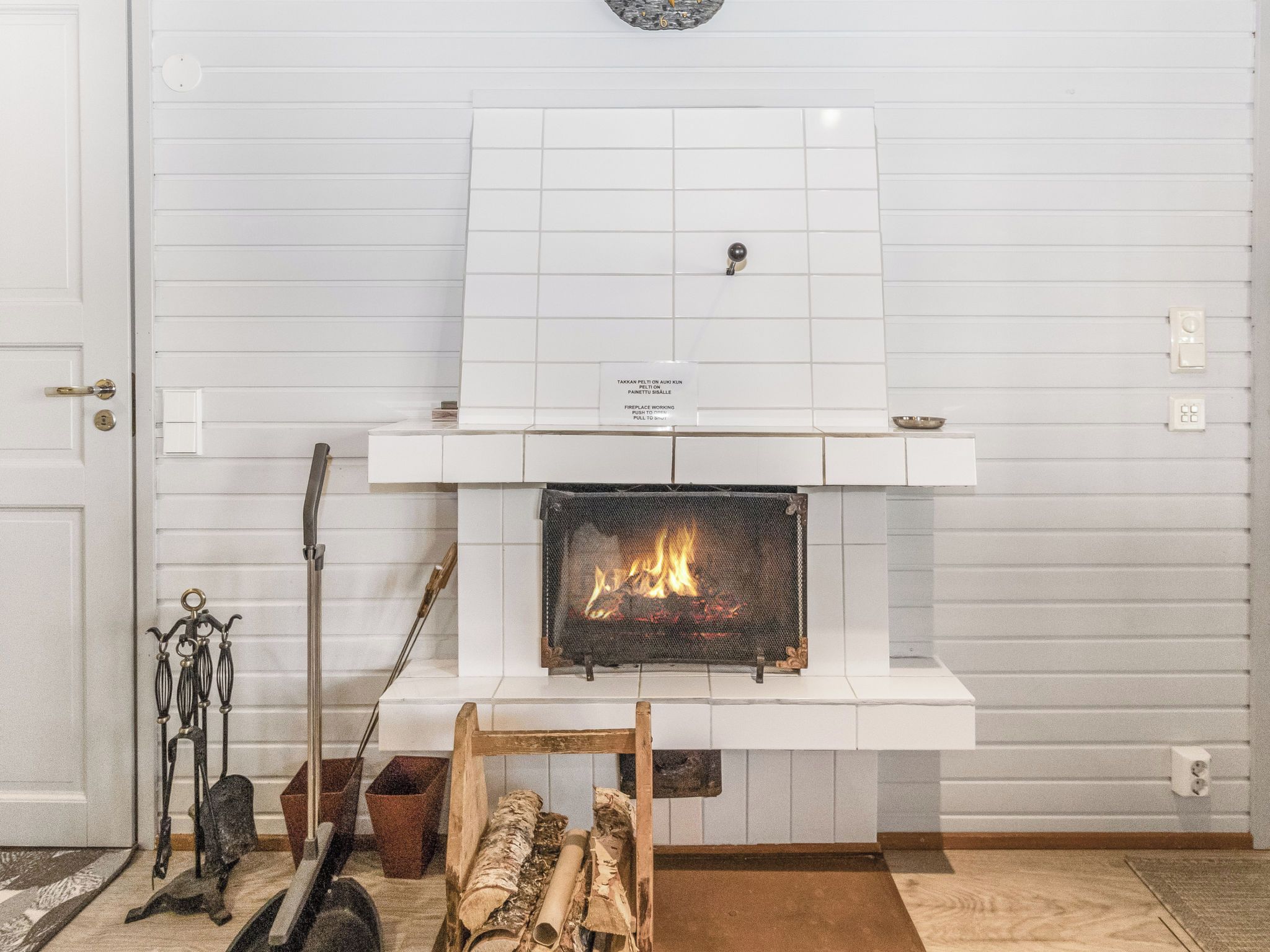 Una chimenea con un revestimiento de azulejos, un cartel encima y leña en el frente.