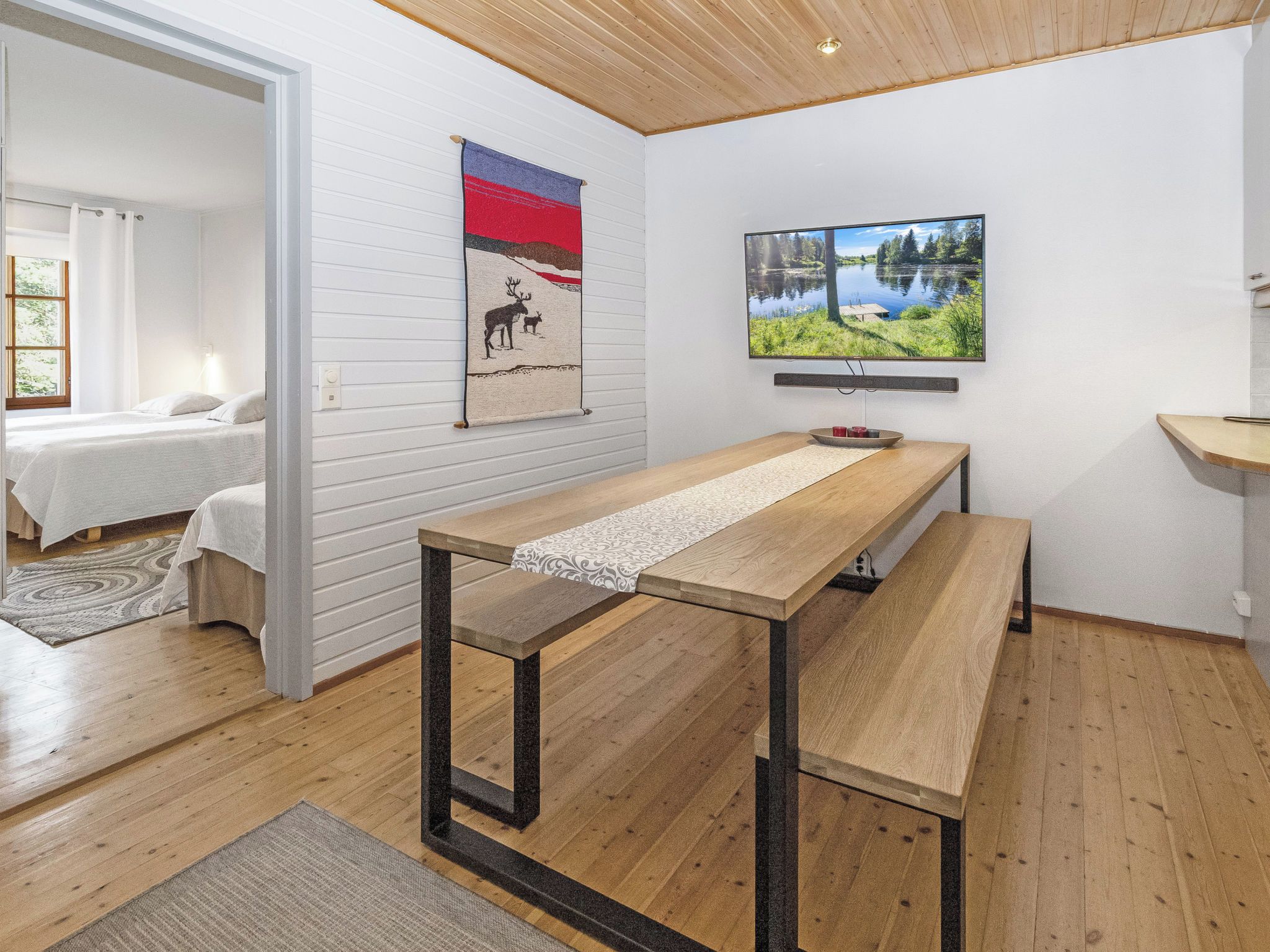A modern room with a wooden table, a bed, and a painting of a lake.