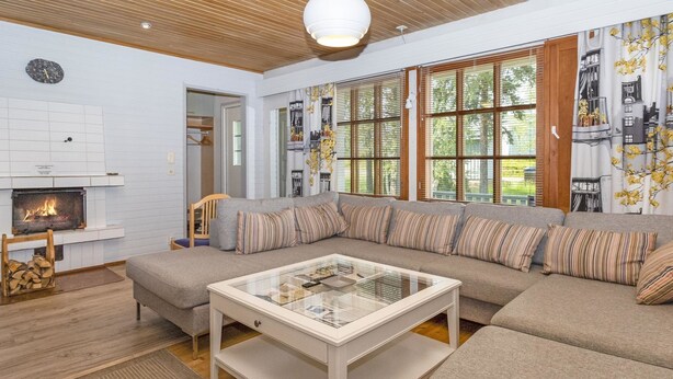 Una sala de estar moderna con un sofá seccional, una mesa de centro de vidrio, una chimenea y ventanas amplias con persianas.