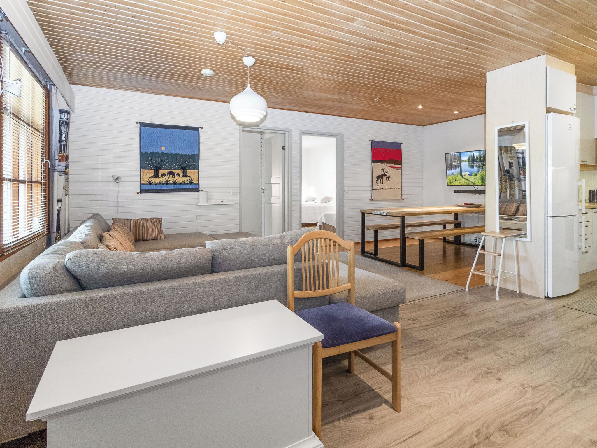 Una sala moderna con un sofá seccional gris, una mesa de comedor de madera y un refrigerador blanco.