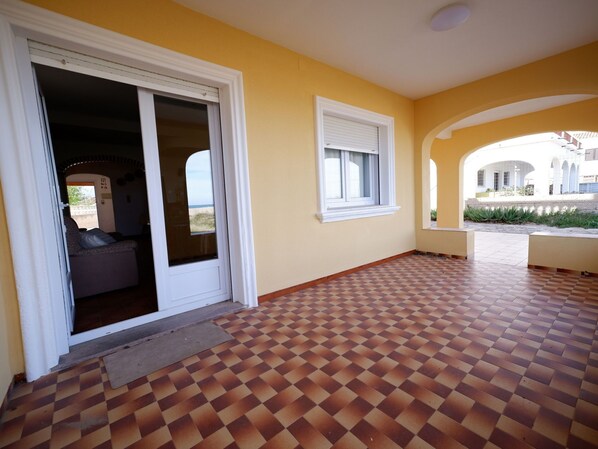 A room with a checkered floor, a sliding glass door, a window with blinds, and a view of the outside.