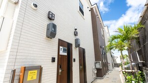Un edificio con dos puertas de madera, un letrero a la izquierda y un pequeño jardín con una palmera.