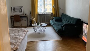 A compact living space with a bed, a green sofa, a small round coffee table, a desk with a chair, and a window with curtains. - Beautiful 1-Bed Apartment in Stockholm (Stockholm)