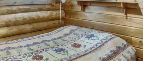 A log cabin room with a bed, a window with curtains, and a framed picture on the wall.