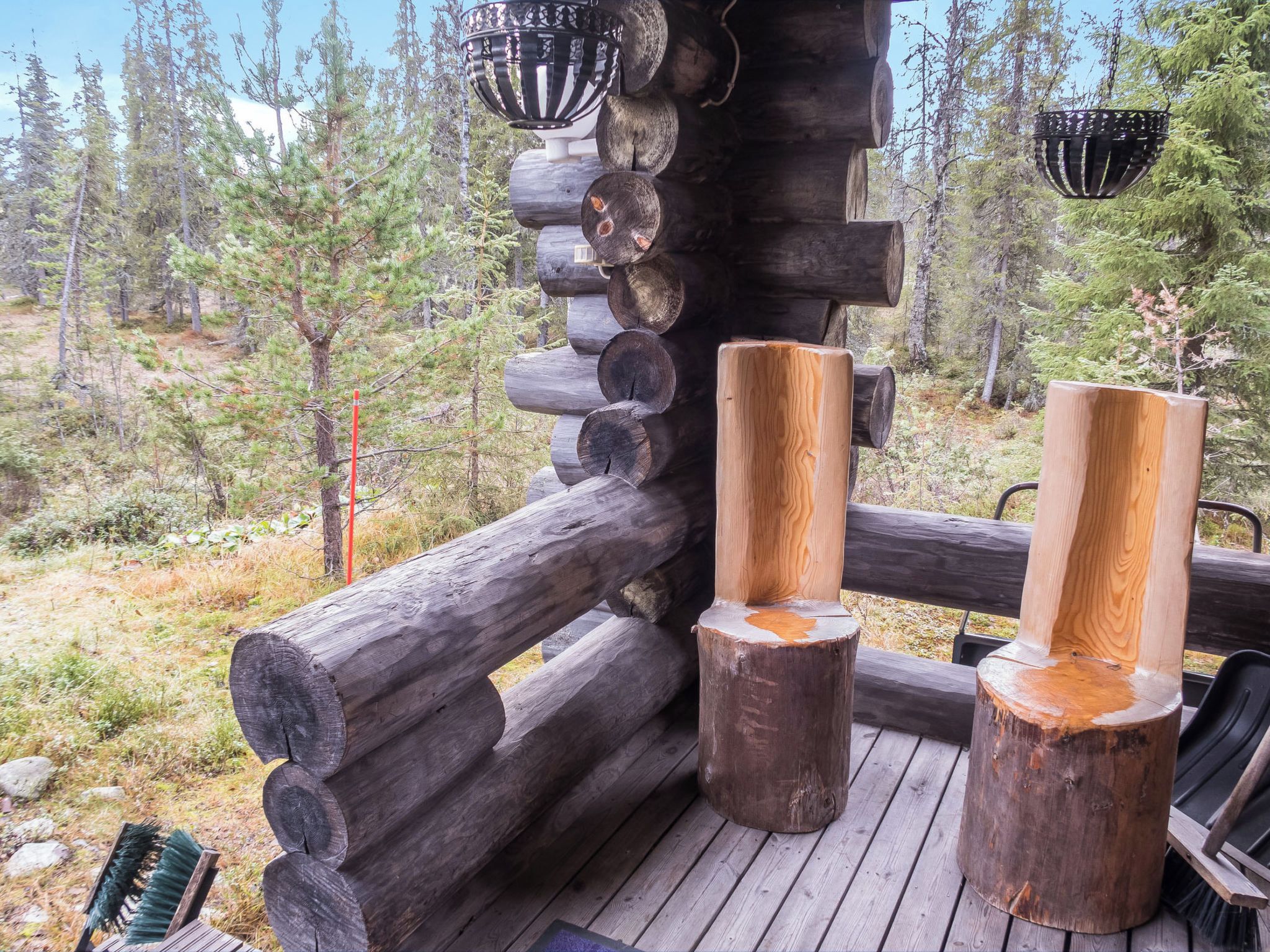 Une terrasse en bois avec une rambarde rustique faite de rondins, un banc et des lanternes suspendues.
