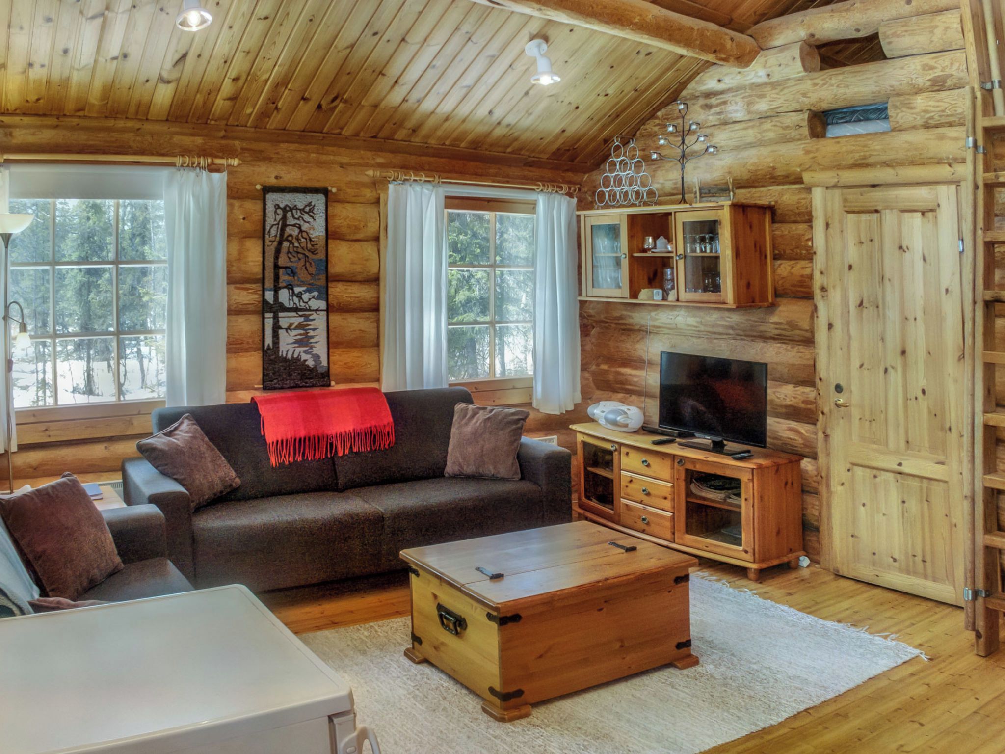 Ein Interieur einer Blockhütte mit einer Couch, einem Fernseher, einem Holzschrank und Kunstwerken an der Wand.