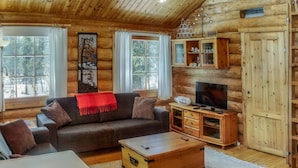 A cozy log cabin interior with a sofa, TV, wooden cabinets, and a large window. - Vuosselin kuukkeli by Interhome (Kuusamo)