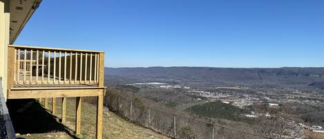A wooden deck with a clear view of a valley and distant buildings.