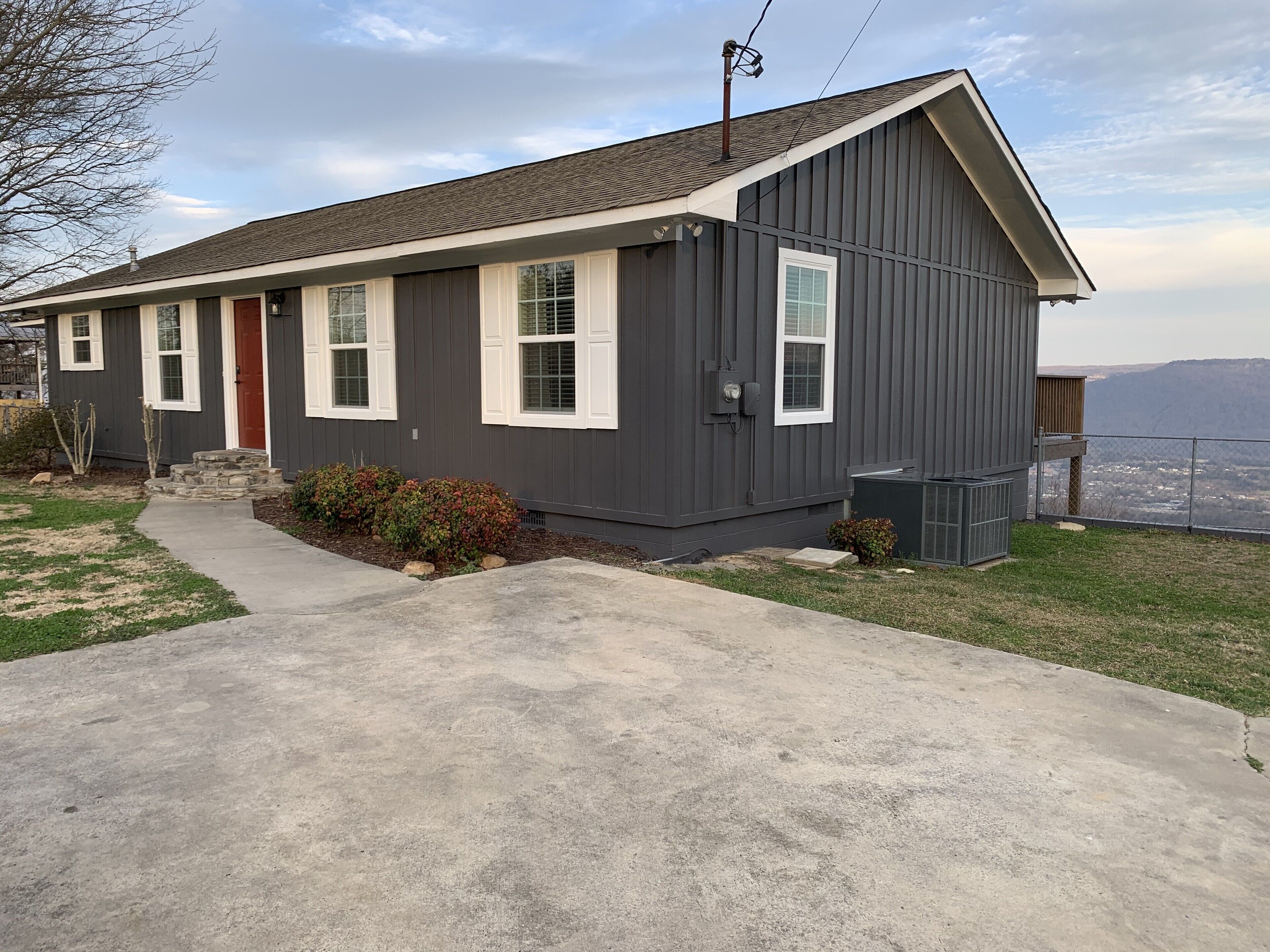 A single-story house with a gray exterior, white trim, and a red door.