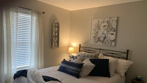 A bedroom with a bed, a nightstand, a lamp, a wall decoration, and a window with curtains. - Mountaintop View (Trenton)
