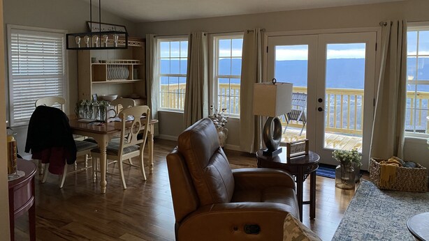 A spacious living room with a leather sofa, dining area with chairs, and a view of the ocean through large windows. - Mountaintop View (Trenton)