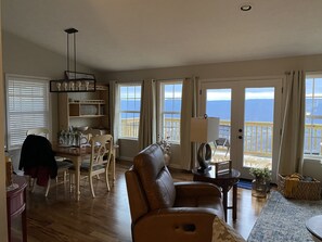 A spacious living room with a leather sofa, dining area with chairs, and a view of the ocean through large windows.