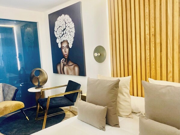A modern hotel room with a bed, a blue wall, a wooden panel wall, a painting, and a round table with a chair.