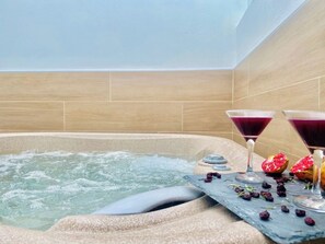 Un jacuzzi con dos vasos de martini llenos de una bebida morada, rodeado de granadas partidas y frutas secas.