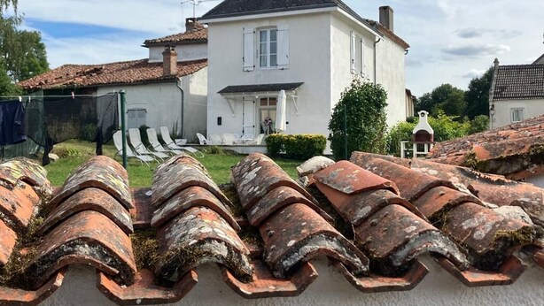 Une maison blanche avec un toit en tuiles, un petit jardin et une clôture.