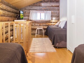 Quarto de cabana de madeira com berço de madeira, uma cama de solteiro, um banquinho pequeno e uma televisão sobre uma estante de madeira.
