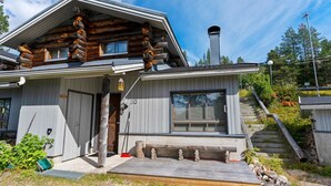 Eine moderne Blockhütte mit großem Fenster, Schornstein und einer Holzterrasse.