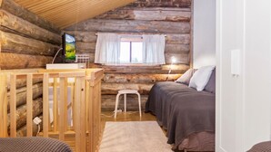 Ein Blockhaus-Zimmer mit einem Holckrippe, einem Bett, einem kleinen Hocker und einem Fenster mit Vorhängen.