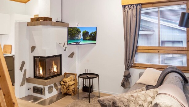 Ein gemütliches Wohnzimmer mit Kamin, einem an der Wand montierten Fernseher und einem Fenster mit Vorhängen.