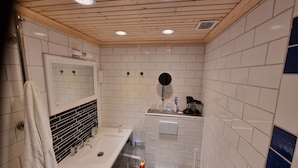 Een moderne badkamer met witte tegels, een houten plafond, een wastafel, een spiegel en een toilet.