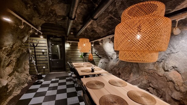 Een restaurant met een schaakbordvloer, lange houten tafels met geweven tafelonderleggers en rustieke stenen muren.