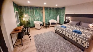Een moderne slaapkamer met een bed, twee stoelen, een bureau en een grote spiegel.