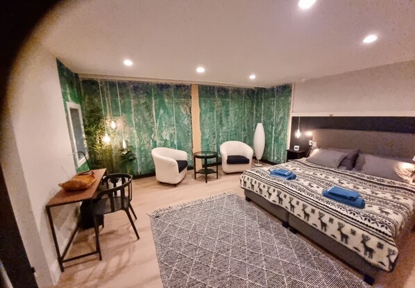 A modern bedroom with a bed, two chairs, a desk, and a large mirror.