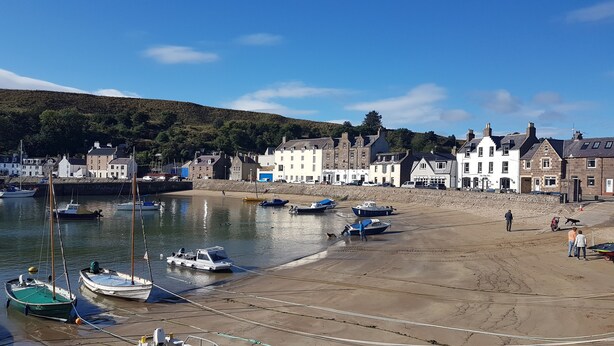 A coastal town with boats docked along the shore, a sandy beach, and buildings with a traditional architectural style.