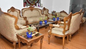 Ein traditionelles Wohnzimmer mit aufwendigen Holzmöbeln, darunter eine Sofagarnitur und passende Sessel, die um einen Glastisch mit Dekoration angeordnet sind.